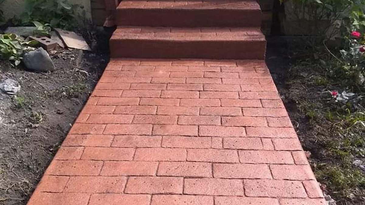 A finished red stamped-concrete walkway in a running brick pattern, leading to matching stamped steps at the side of a house.