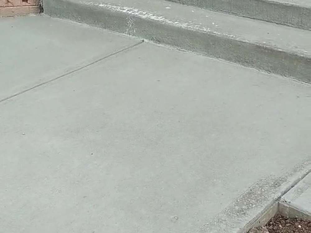 A set of freshly poured plain concrete entry steps against the brick wall of a house, next to a doorway.